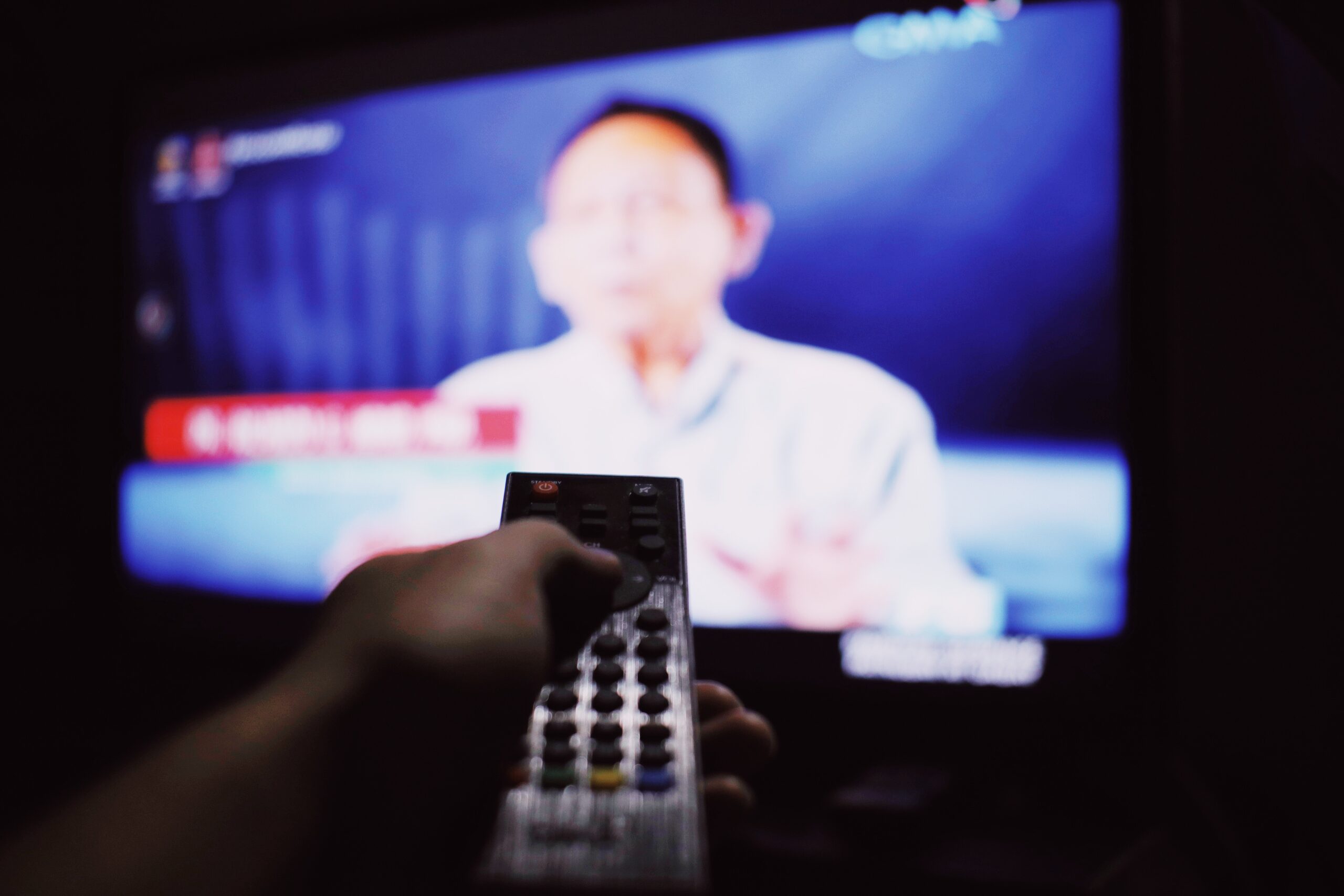Close up of a hand pointing a remote control at a TV