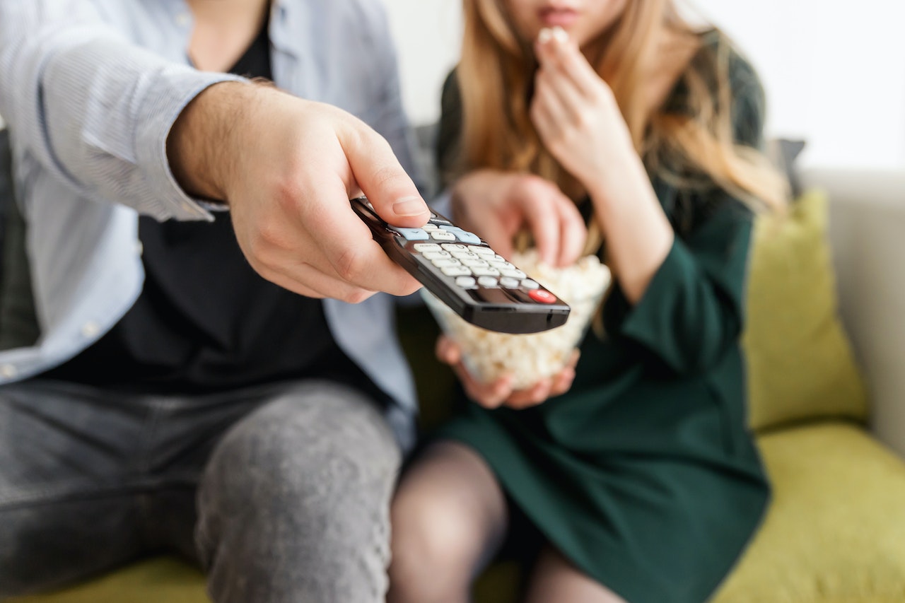 A man pointing a remote while watching TV with a woman